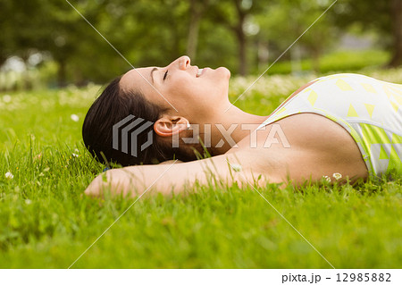 Peaceful fit brunette lying on the grass 12985882