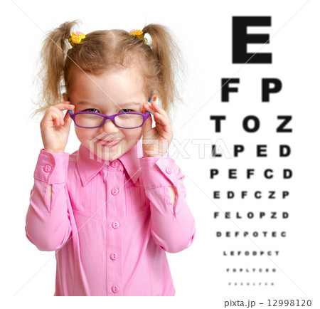 Smiling girl putting on glasses with blurry eye chart behind her 12998120