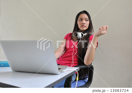A young and beautiful Asian female student pondering / brainstorming at her desk in front of laptop 13063724