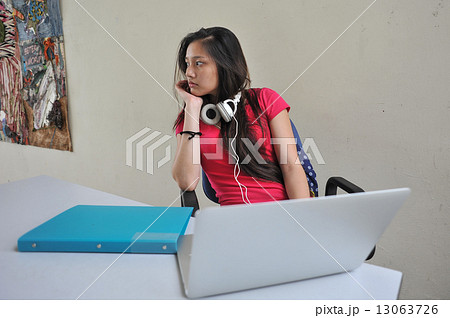 A young and beautiful Asian female student pondering / brainstorming at her desk in front of laptop 13063726