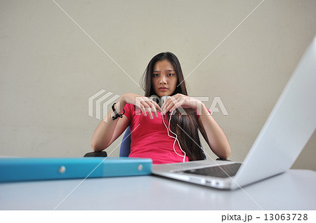 A young and beautiful Asian female student pondering / brainstorming at her desk in front of laptop A young and beautiful Asian female student pondering / brainstorming at her desk in front of laptop 13063728