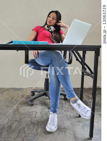 A young and beautiful Asian female student pondering / brainstorming at her desk in front of laptop 13063729