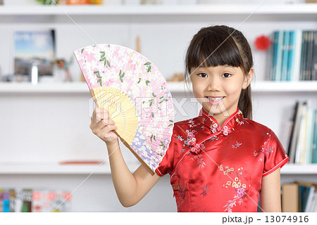 Little Chinese girl in Cheongsam with Chinese Fan in front of bookshelf 13074916