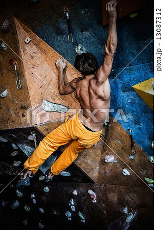 Muscular man practicing rock-climbing on a rock wall indoors 13087312