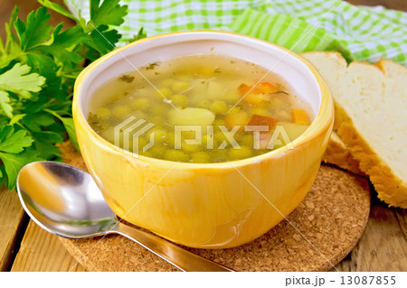 Soup of green peas in yellow bowl with bread on board 13087855