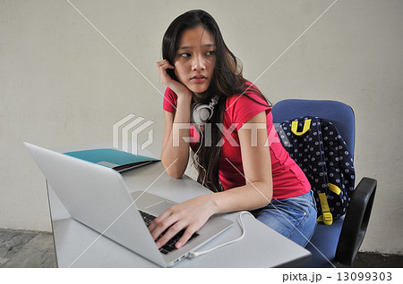 A young beautiful Asian female student looking restless seated at her desk in front of laptop A young beautiful Asian female student looking restless seated at her desk in front of laptop 13099303