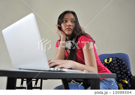 A young beautiful Asian female student looking restless seated at her desk in front of laptop A young beautiful Asian female student looking restless seated at her desk in front of laptop 13099304
