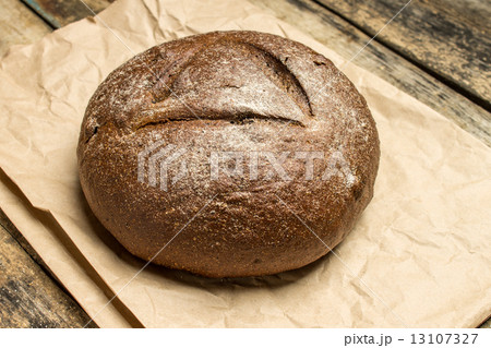Fresh baked loaf of bread on paper bag at wooden table 13107327