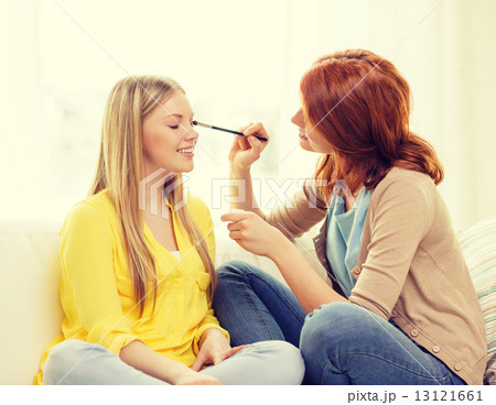 two smiling teenage girls applying make up at home 13121661