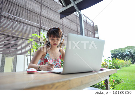 A lovely young Asian lady wearing headphone listening to music while doing her work at a campus desk 13130850