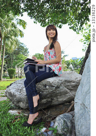 A portrait of young and beautiful Asian lady using her tablet relaxing in the garden A portrait of young and beautiful Asian lady using her tablet relaxing in the garden 13136229