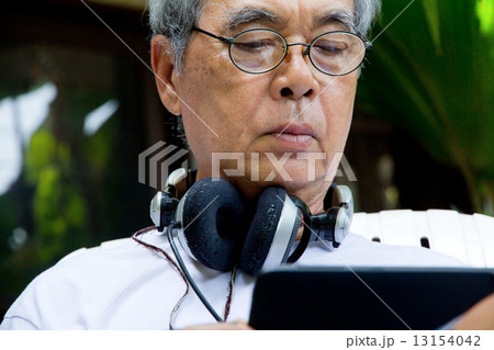 Senior man sitting outside reading E-book on his tablet.  13154042