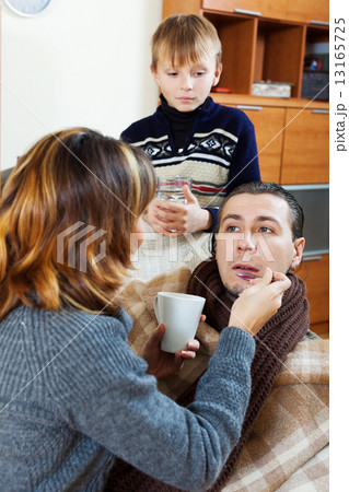 Woman and son giving medicinal syrup to sick man 13165725