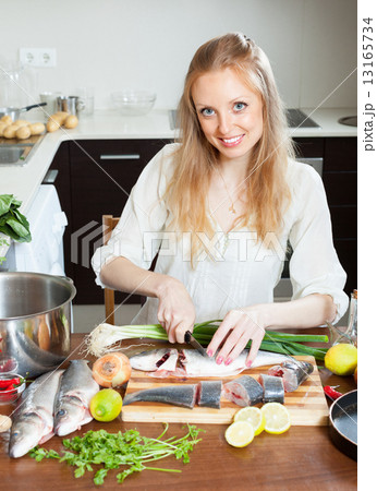 positive woman slicing raw fish at kitchen table 13165734