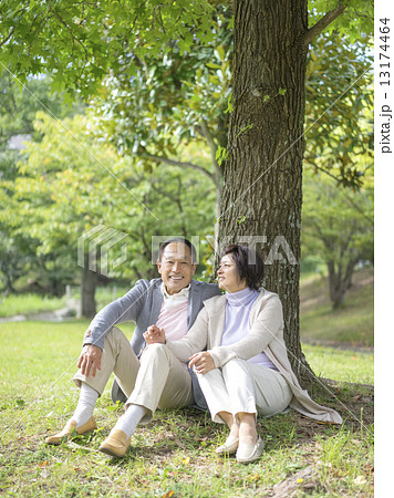 木にもたれて座る中高年夫婦の写真素材