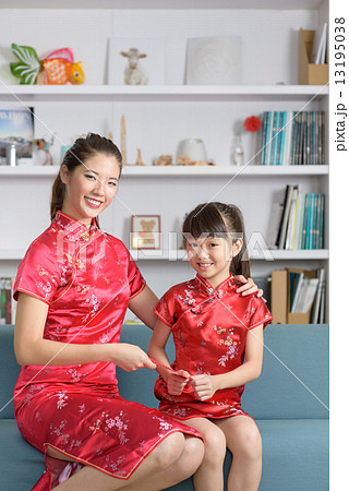 Young Chinese mother in cheongsam giving daughter red packet during lunar new year in living room Young Chinese mother in cheongsam giving daughter red packet during lunar new year in living room 13195038