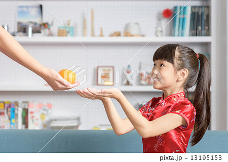 Little Chinese girl in cheongsam receiving oranges during lunar new year in living room  13195153