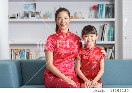 Young chinese mother and daughter in cheongsam sitting together in the living room 13195189