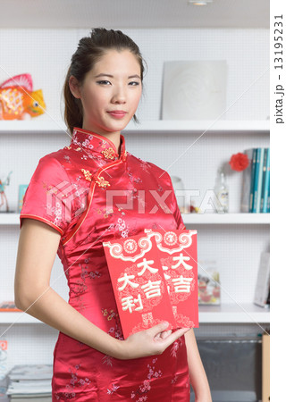 One young Chinese woman in cheogsam holding 2 big red packet in front of bookshelf 13195231