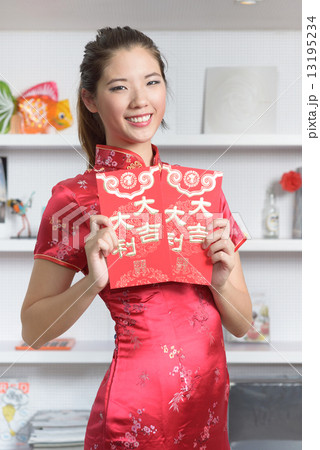 One young Chinese woman in cheogsam holding 2 big red packet in front of bookshelf One young Chinese woman in cheogsam holding 2 big red packet in front of bookshelf 13195234