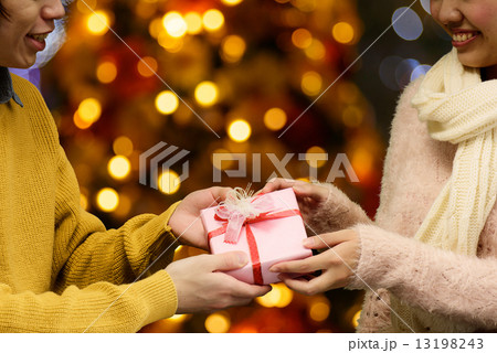 イルミネーションが綺麗なところでプレゼント交換する男女のてのアップの写真素材