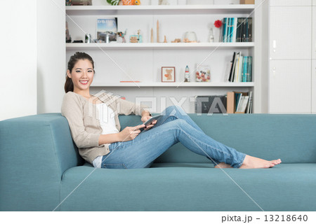 One young chinese woman using mobile device tablet iPad relaxing on a sofa 13218640