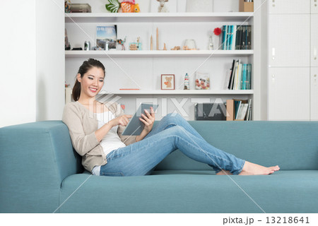 One young chinese woman using mobile device tablet iPad relaxing on a sofa 13218641