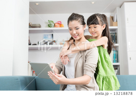 Young chinese daughter hugging mother as she is using mobile device tablet iPad in the living room 13218878