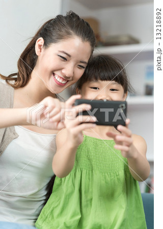 Young chinese mother and daughter taking selfies using mobile device smart phone in the living room 13218892