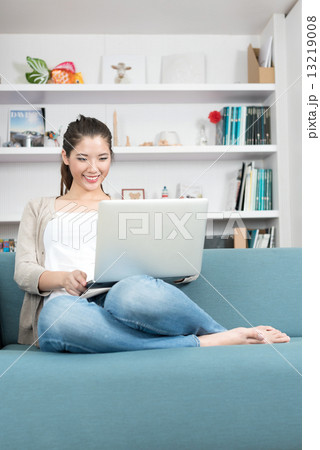 One young chinese woman using mobile device laptop relaxing on a sofa 13219008