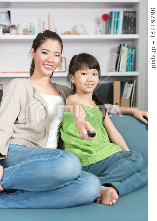 Young chinese daughter changing TV channel while watching with mother at home 13219790