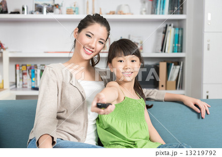 Young chinese daughter changing TV channel while watching with mother at home 13219792