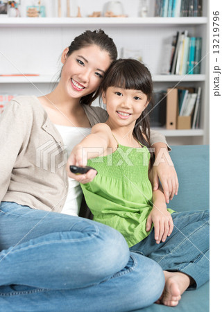 Young chinese daughter changing TV channel while watching with mother at home 13219796
