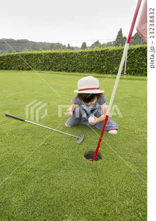 Young girl sitting by a golf course hole. 13238832