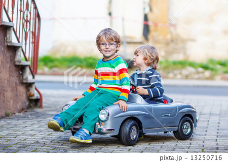 Two happy kids playing with big old toy car in summer garden, ou Two happy kids playing with big old toy car in summer garden, ou 13250716