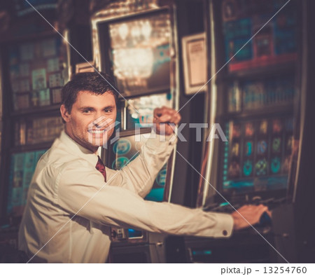 Handsome happy brunette man in white shirt near slot machine 13254760