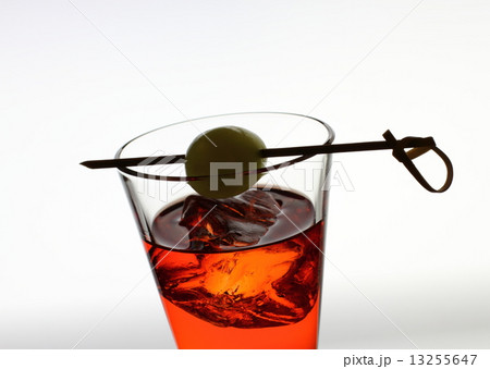 Short drink glass with red liquid, olive, ice cubes 13255647