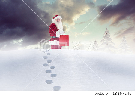 Composite image of santa carrying gifts in the snow 13267246