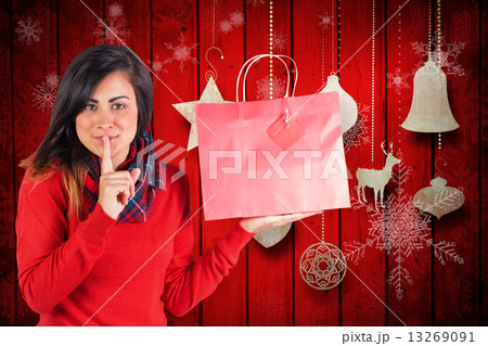 Composite image of brunette holding gift bag and keeping a secre 13269091