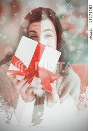 Composite image of brunette showing gift on the couch at christm 13271562