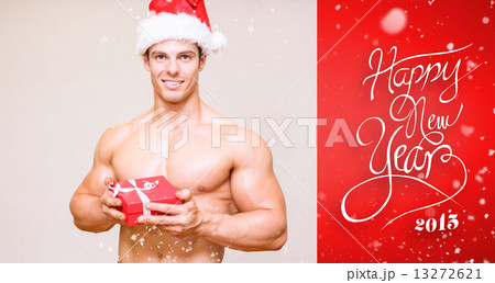Composite image of shirtless macho man in santa hat holding gift 13272621