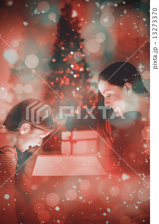 Composite image of festive mother and daughter opening a glowing 13273370