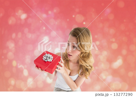 Composite image of surprised woman holding a gift 13277290