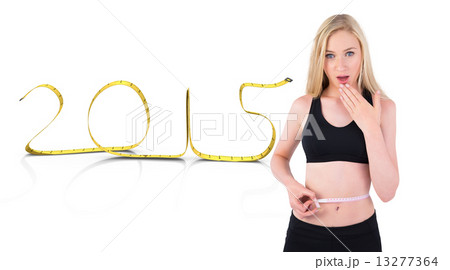 Composite image of fit young blonde looking at measuring tape 13277364