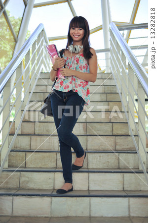 A young and beautiful Asian female student carrying books and walking down stairways smiling A young and beautiful Asian female student carrying books and walking down stairways smiling 13282818