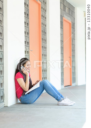 One young pan asian female student making a call while studying along campus corridor 13310040