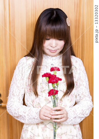 木の壁の前でカーネーションの花を持つ女性 13320302