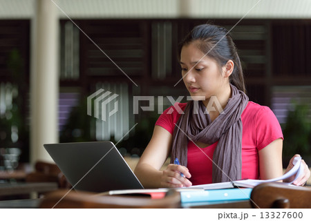 One young pan asian female student studying hard for examination in campus cafe 13327600