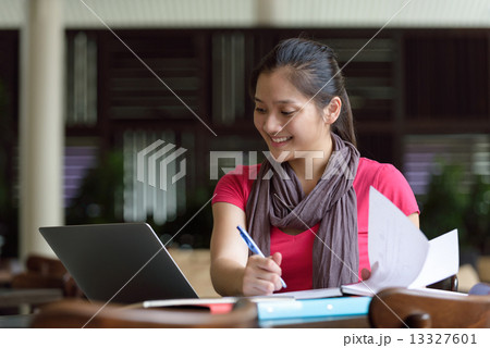 One young pan asian female student studying hard for examination in campus cafe 13327601