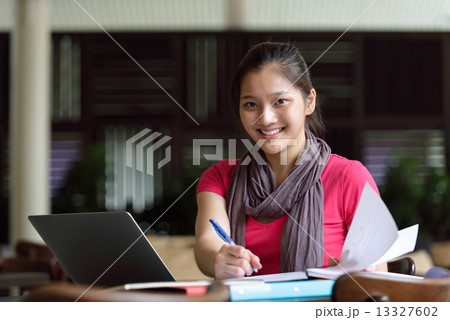 One young pan asian female student studying hard for examination in campus cafe 13327602